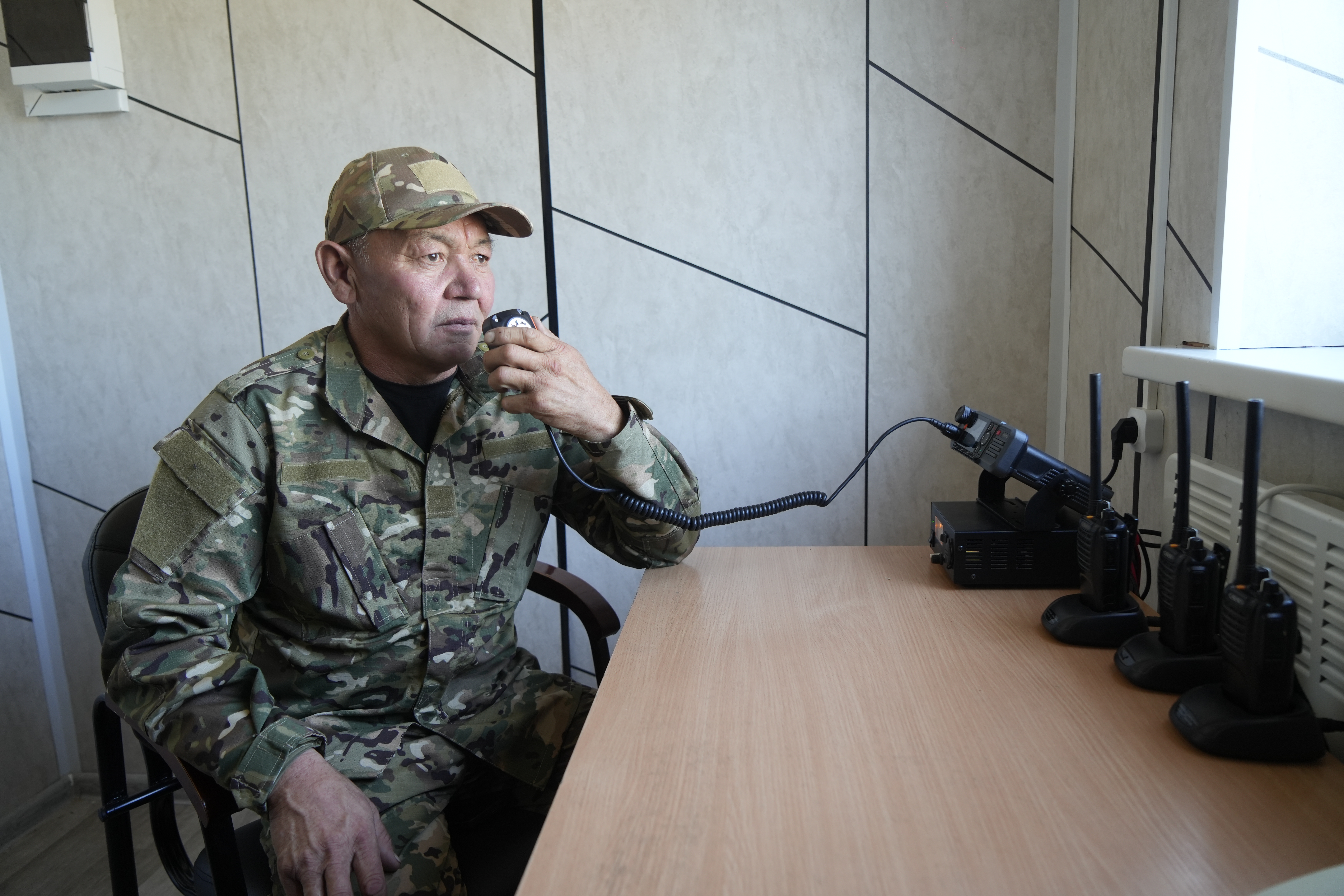 Камуфляж киген әскери адам үстел басында радиостанция арқылы сөйлесіп жатыр.