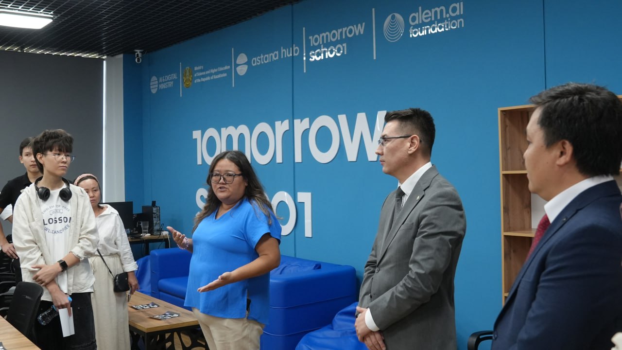 Astana Hub және Tomorrow School кеңсесіндегі кездесу. Көк фон алдында тұрған адамдар.