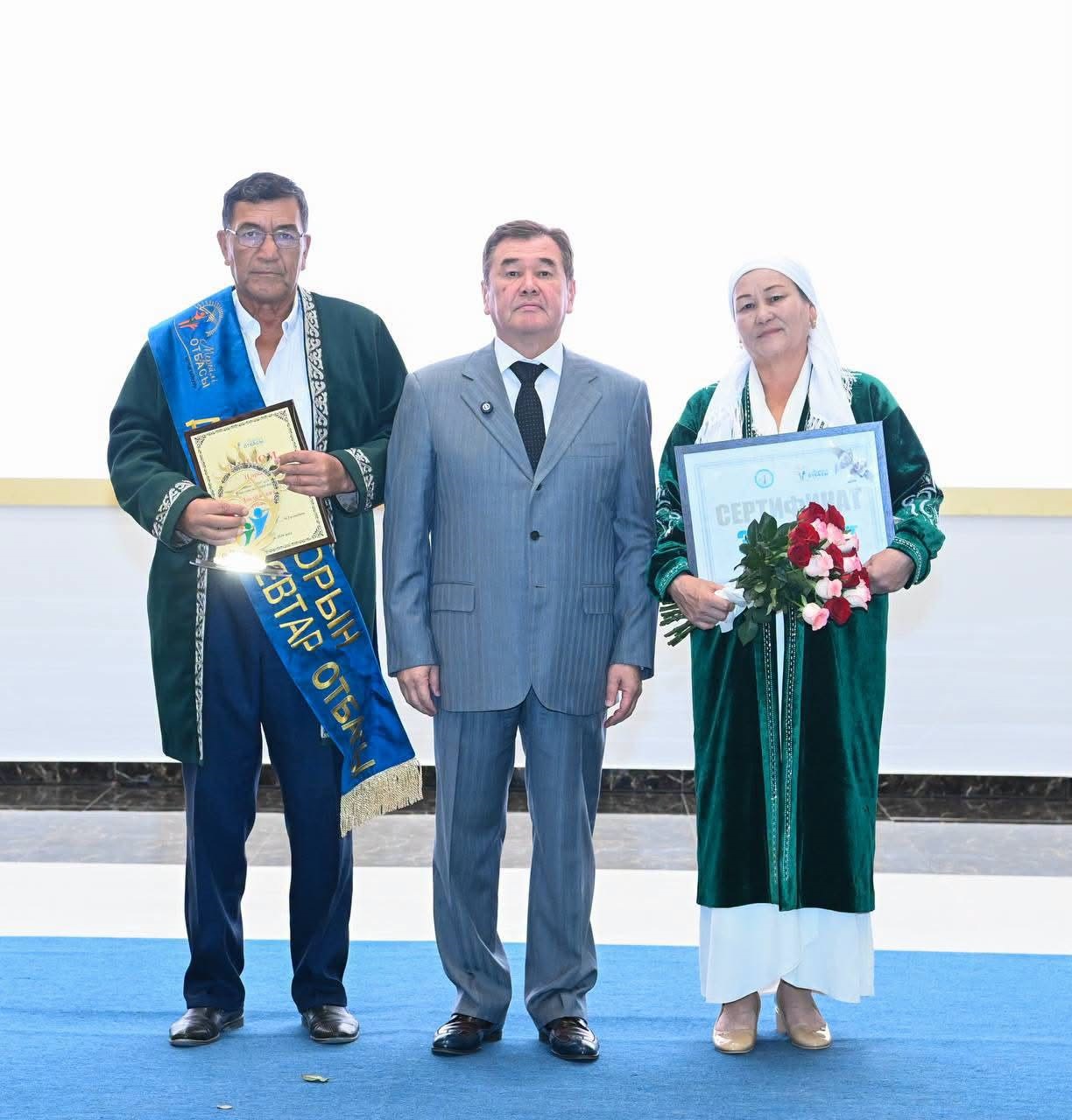 Марапат алған жұп пен костюм киген ер адамның бірге түскен суреті.