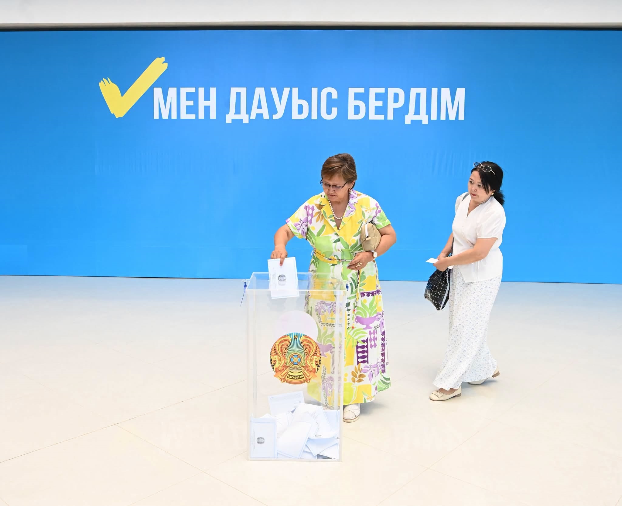 Сайлау участке әйел адамның дауыс қорабына бюллетень салуы. Фонда «Мен дауыс бердім» деген жазу бар.