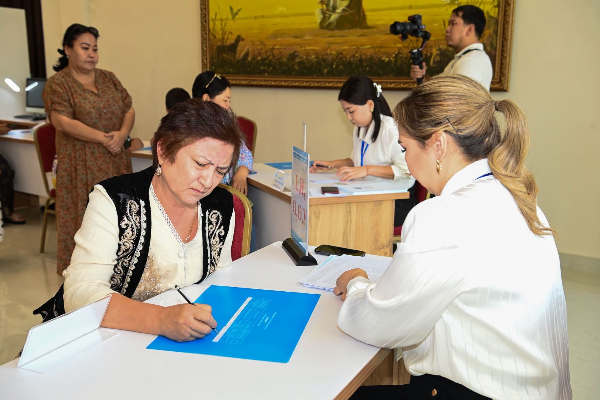 Келісімшартқа қол қойып жатқан әйел және оған көмектесіп тұрған қызметкер.