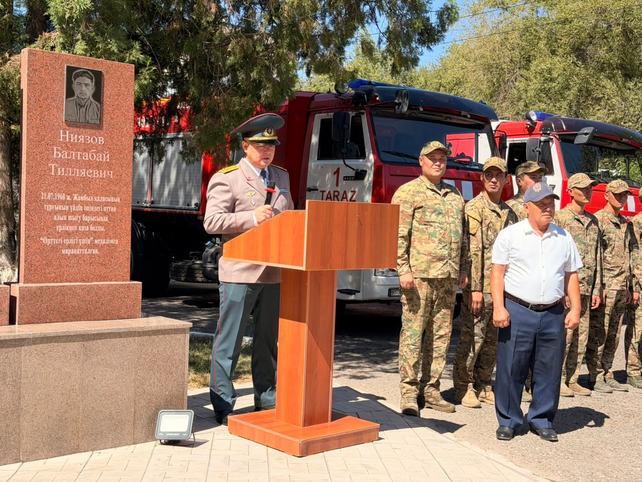 Өрт сөндірушілердің ескерткіші алдында сөйлеп тұрған офицер және әскери қызметшілер.