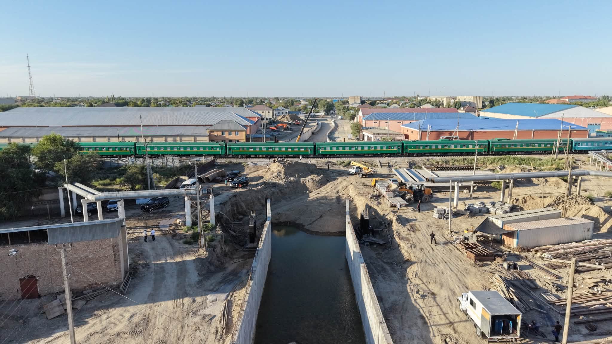 Құрылыс алаңының жанынан өтіп жатқан жасыл жолауын вагондары бар пойыз.