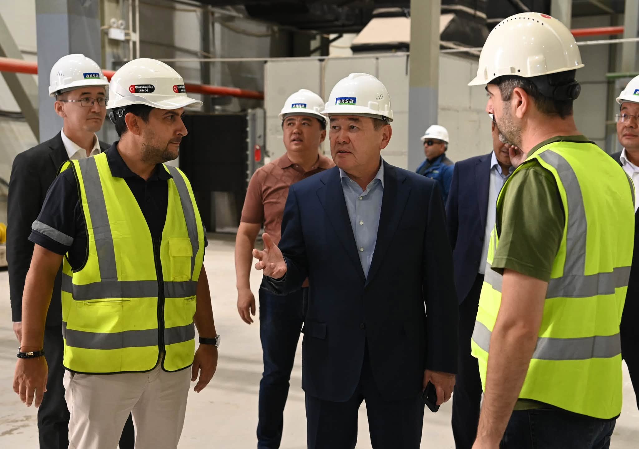 Құрылыс алаңында  мамандар мен ресми киінген ер адамның әңгімелесуі.