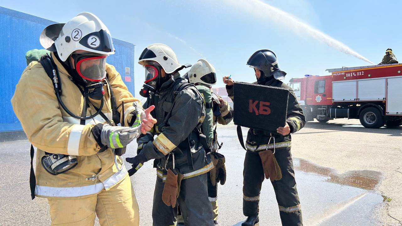 Арнайы киімі мен жабдығы бар өрт сөндірушілердің жаттығу кезіндегі суреті.
