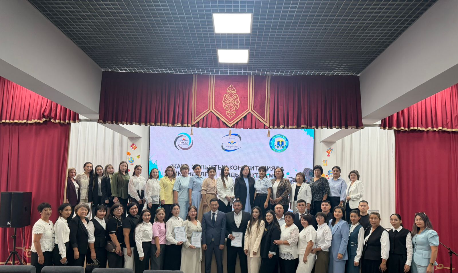 Сахнада жиналған студенттер мен оқытушылардың топтық суреті.