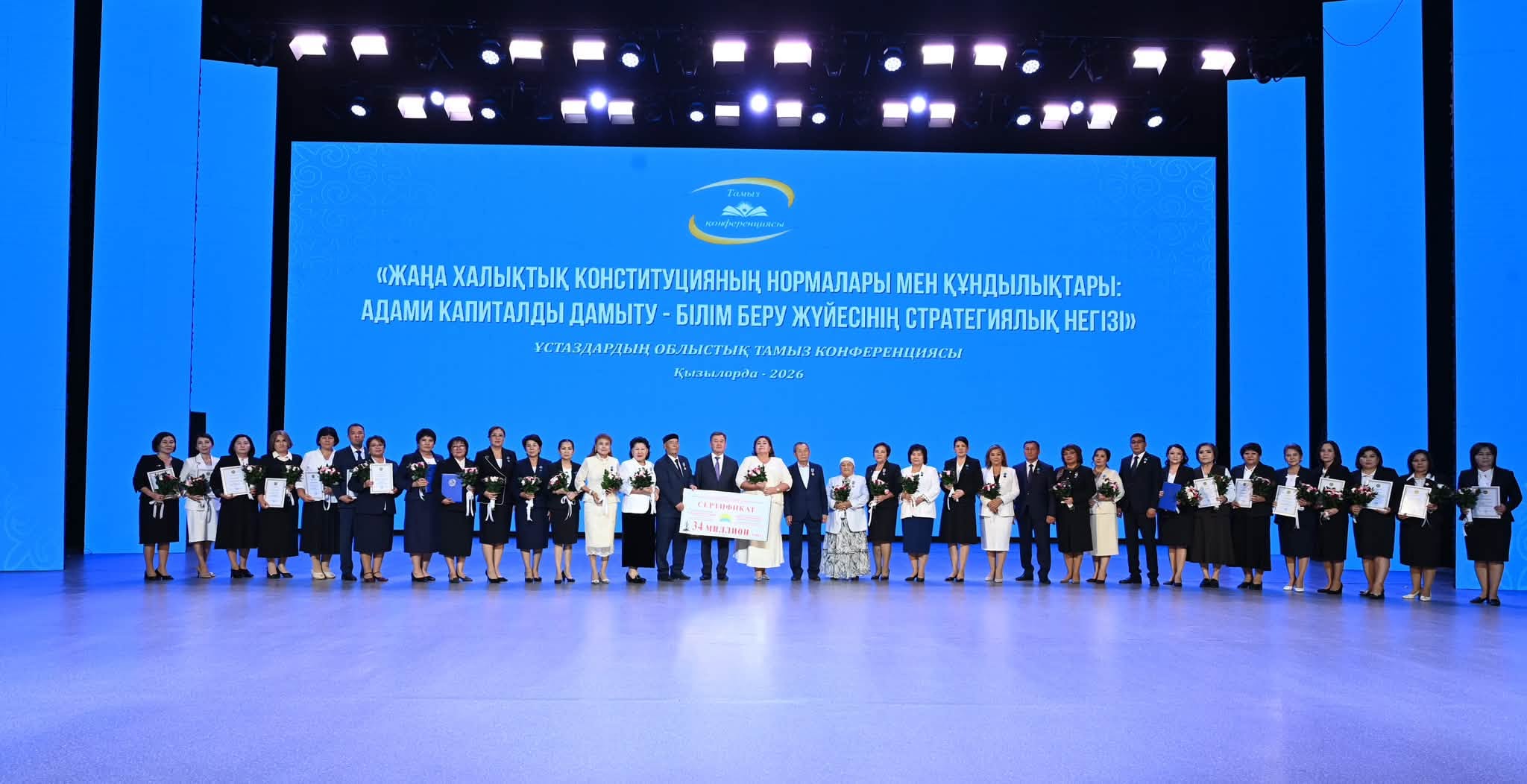 Кызылордада өткен ұстаздардың облыстық тамыз конференциясының қатысушылары сахнада топтық суретке түсуде.