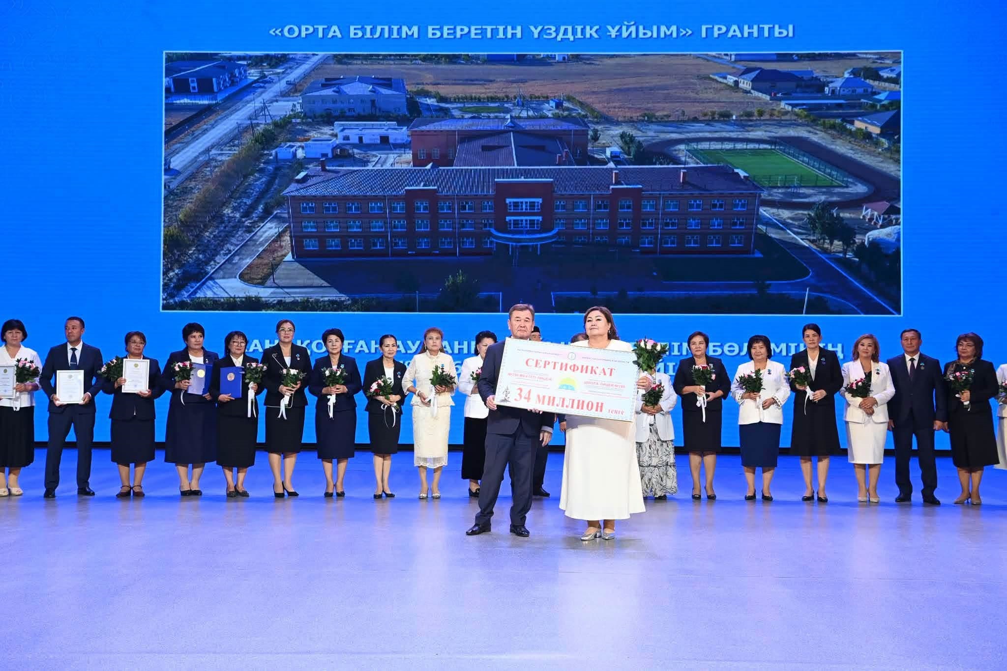 «Орта білім беретін үздік ұйым» грантының табыстау рәсімі: сахнада сертификат ұстаған адамдар мен мұғалімдер тобы.