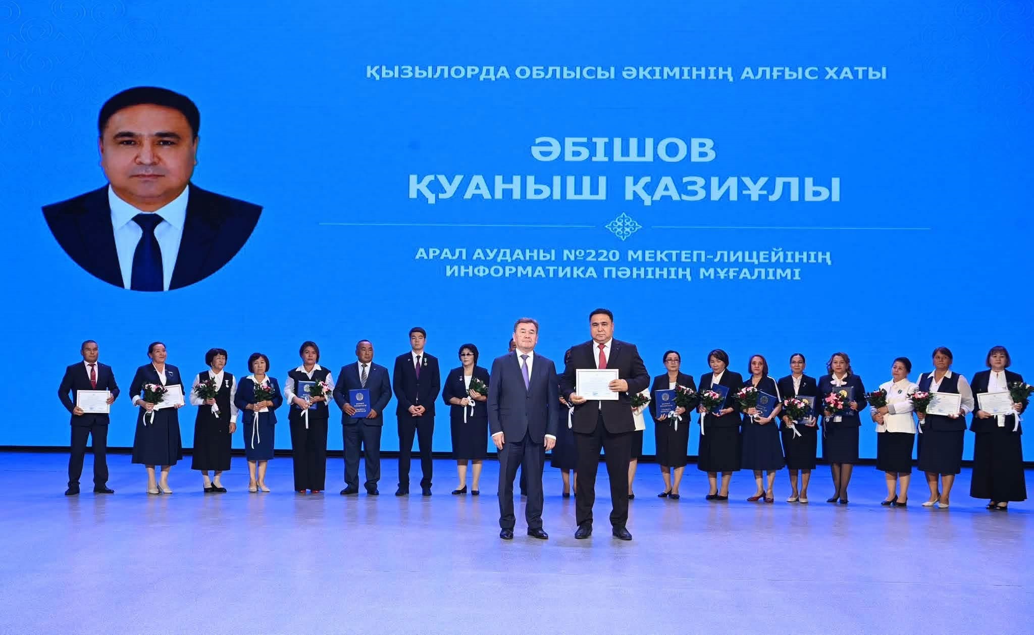 Қызылорда облысы әкімінің алғыс хатын алған мұғалімдер мен қонақтардың сахнадағы топтық суреті.
