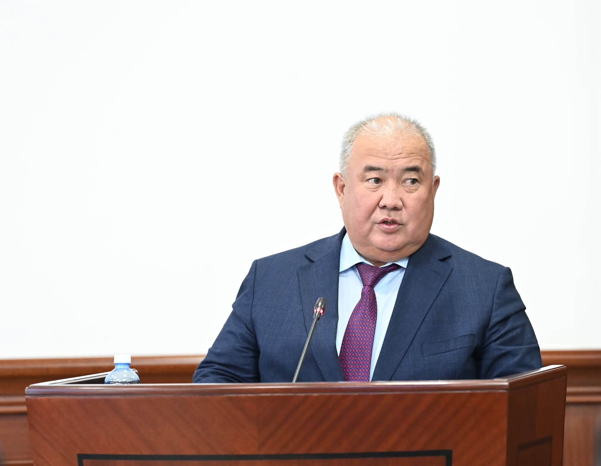 Көк костюм киген ер адам трибунада сөйлеп тұр.