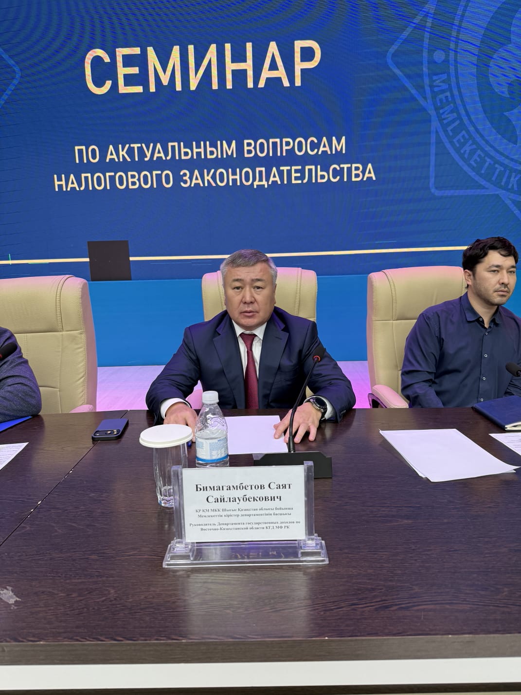Суретте салық заңнамасының өзекті мәселелеріне арналған іскерлік семинар бейнеленген. Іс-шараның атмосферасы ресми әрі іскерлік сипатта. Қатысушылар кәсіби мәселелерді талқылап, пікір алмасуда.